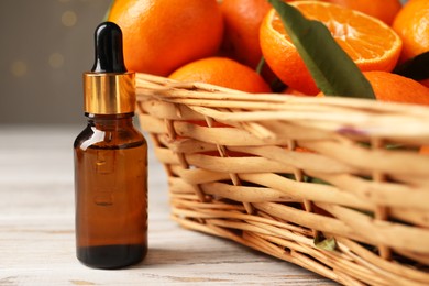 Bottle of tangerine essential oil and fresh fruits on white wooden table, closeup