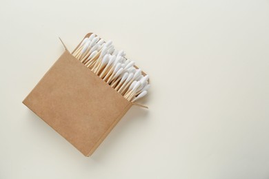 Photo of Box with wooden cotton buds on beige background, top view. Space for text