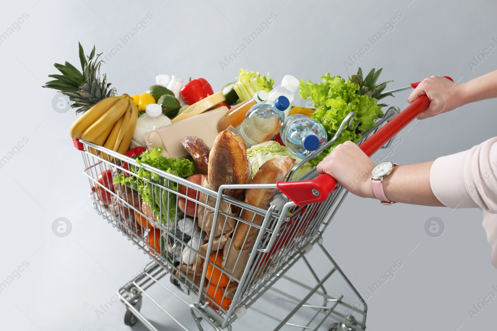 Photo of Woman with shopping cart full of groceries on grey background, closeup