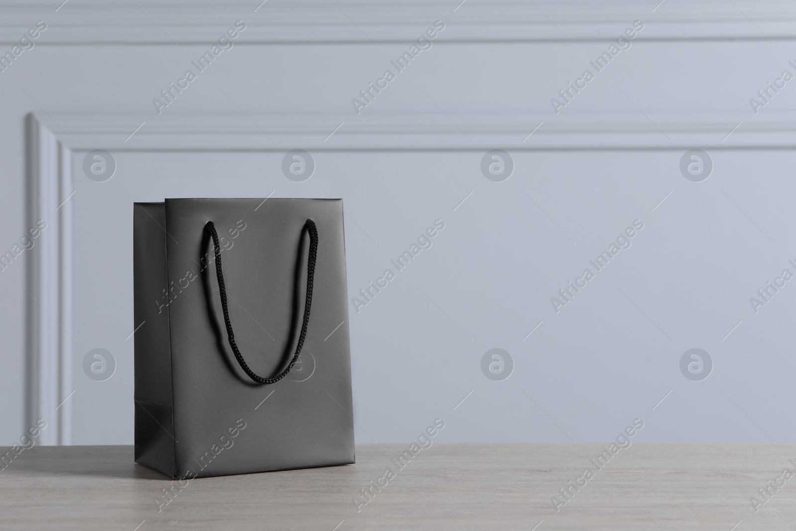 Photo of Black paper bag on wooden table against light grey wall, space for text