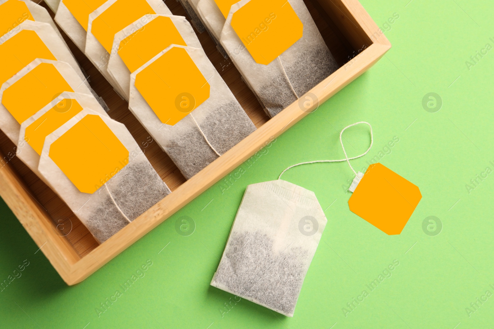 Photo of Many tea bags in wooden box on light green background, flat lay