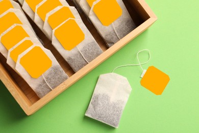 Photo of Many tea bags in wooden box on light green background, flat lay