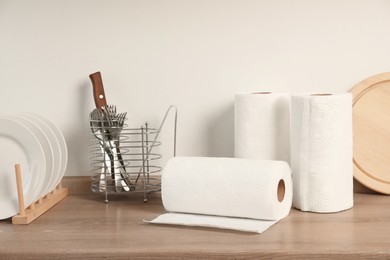 Photo of Many rolls of white paper towels and other kitchen stuff on wooden countertop near light wall