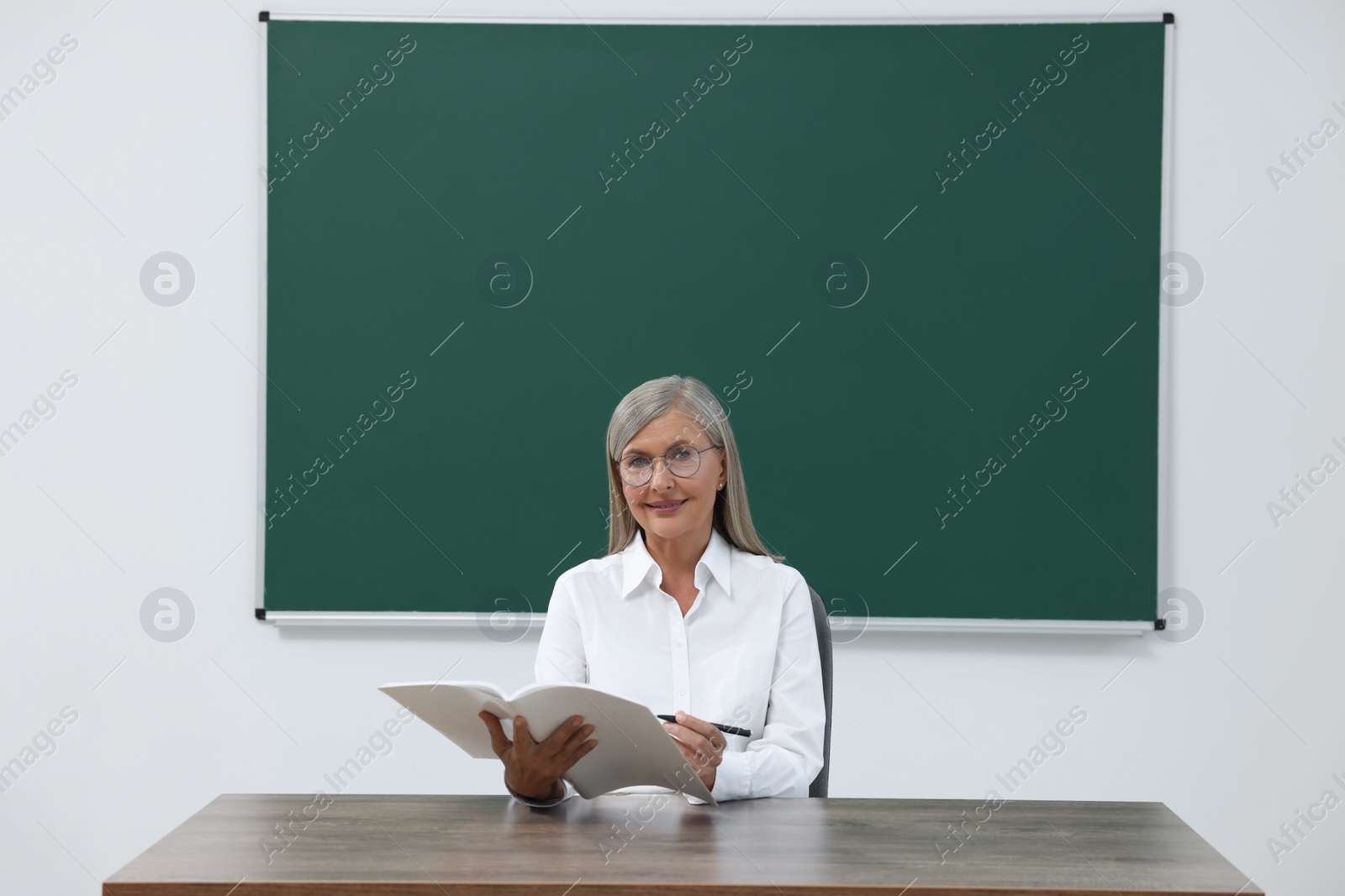 Photo of Professor with notebook and pen sitting at desk in classroom