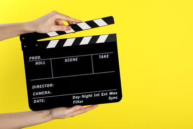 Photo of Woman holding movie clapper on yellow background, closeup. Space for text