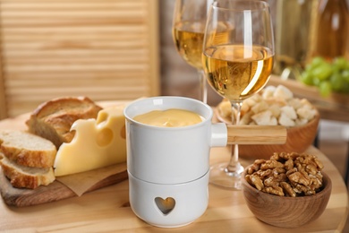 Pot of tasty cheese fondue and products on wooden table