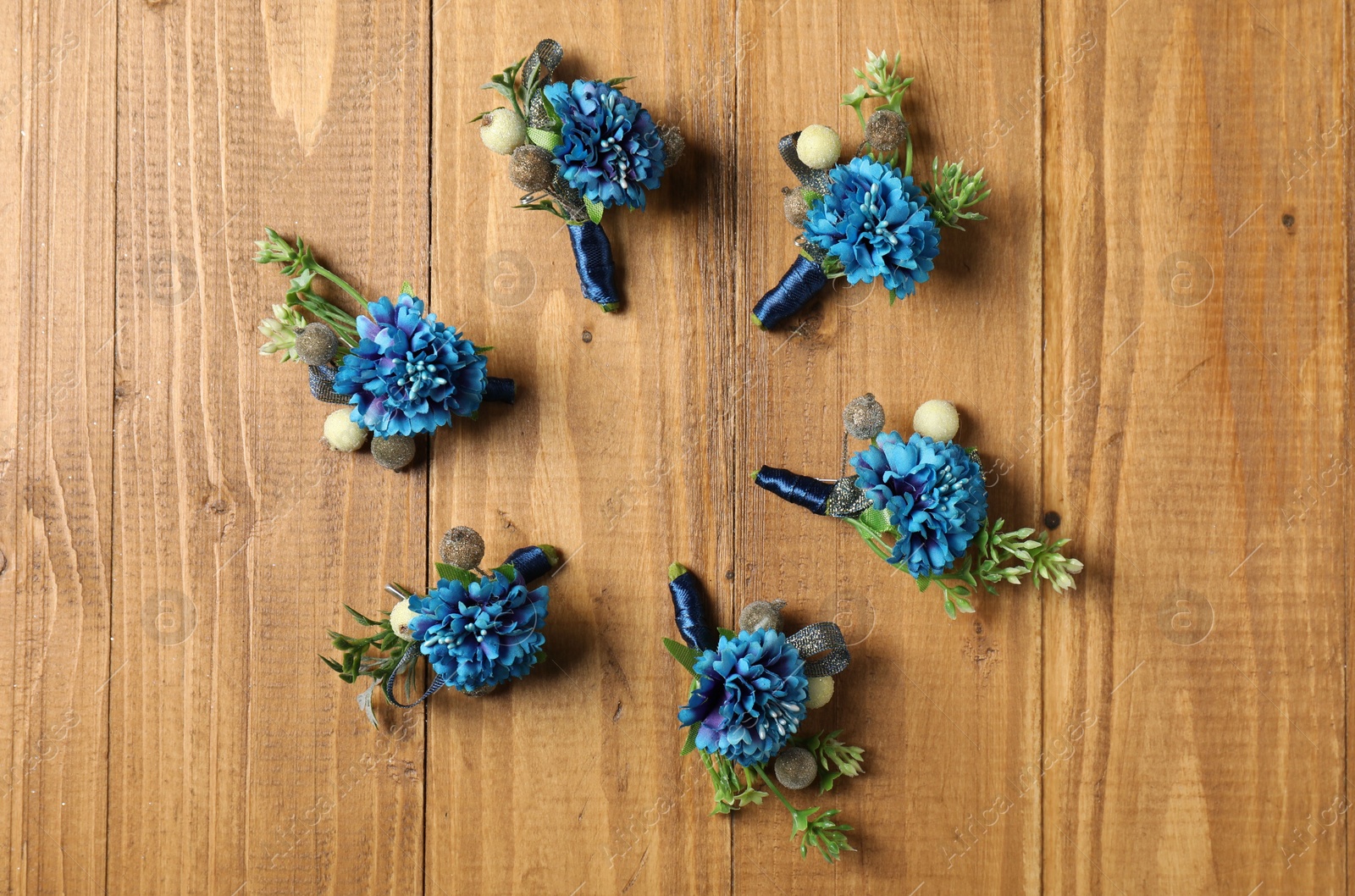 Photo of Stylish blue boutonnieres on wooden table, flat lay