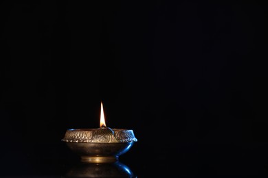 Lit diya on black background, space for text. Diwali lamp