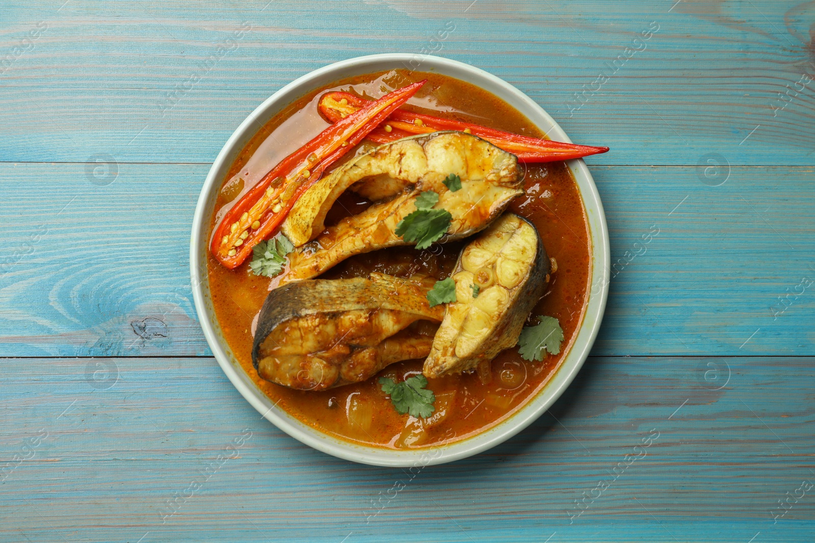 Photo of Tasty fish curry on light blue wooden table, top view. Indian cuisine