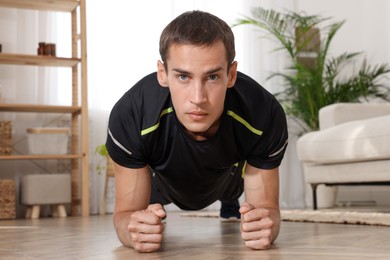 Handsome man doing plank exercise on floor at home