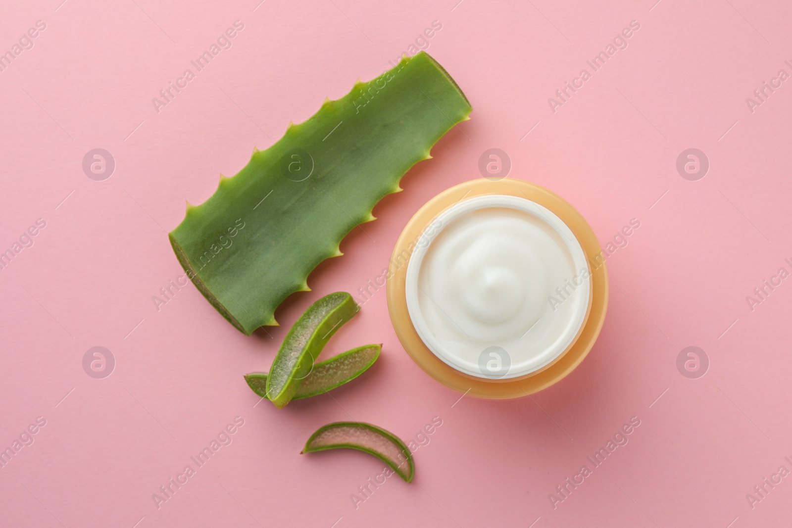 Photo of Jar with cream and cut aloe leaf on pink background, flat lay