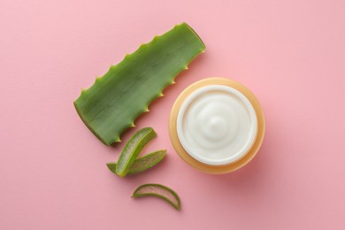 Jar with cream and cut aloe leaf on pink background, flat lay