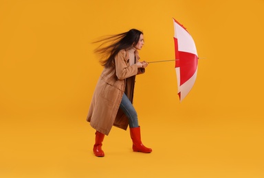 Woman with umbrella caught in gust of wind on yellow background