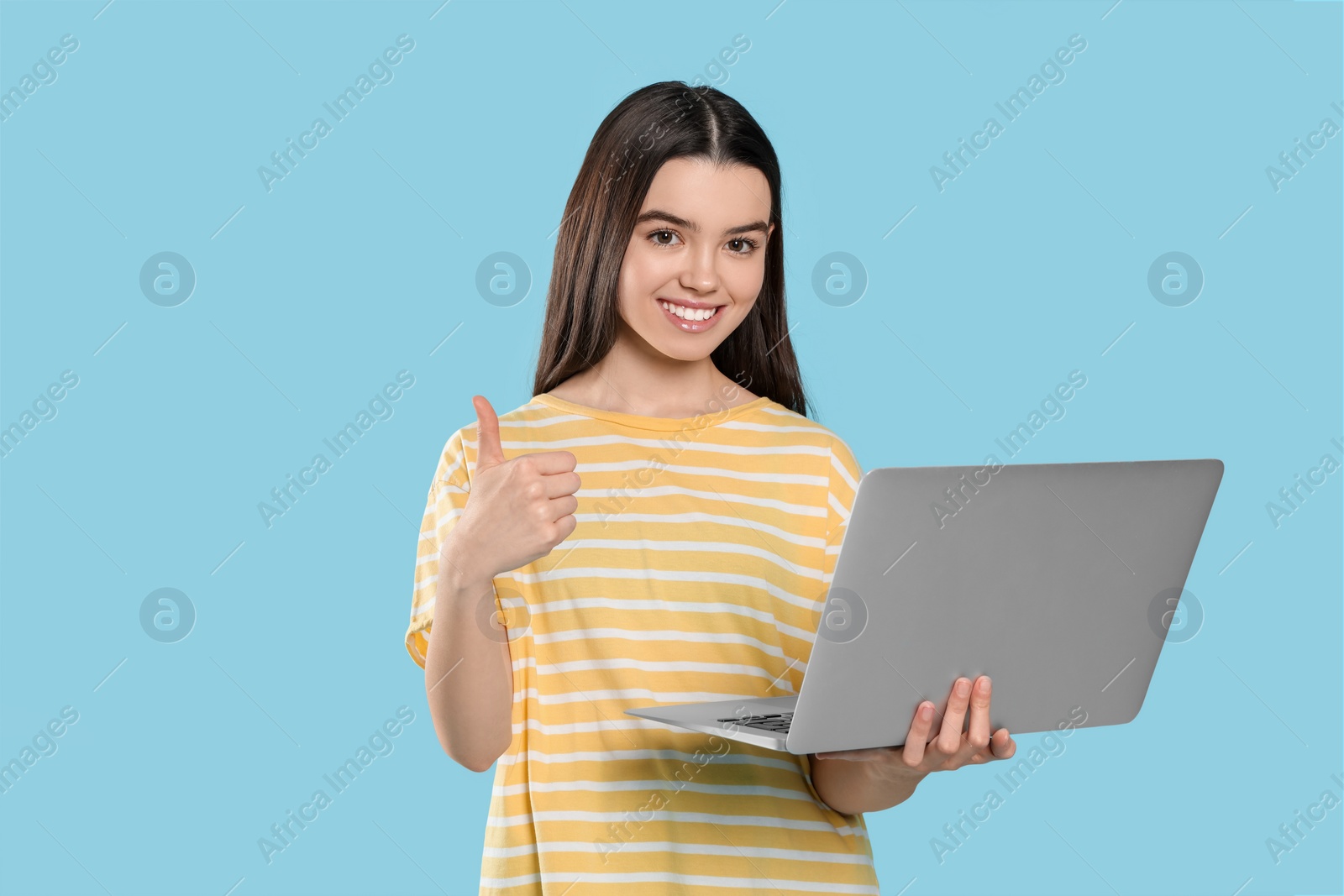 Photo of Teenage girl with laptop showing thumb up on light blue background