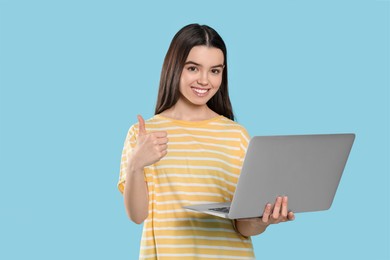 Teenage girl with laptop showing thumb up on light blue background