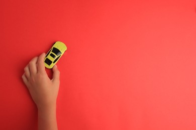 Child playing with toy car on red background, top view. Space for text