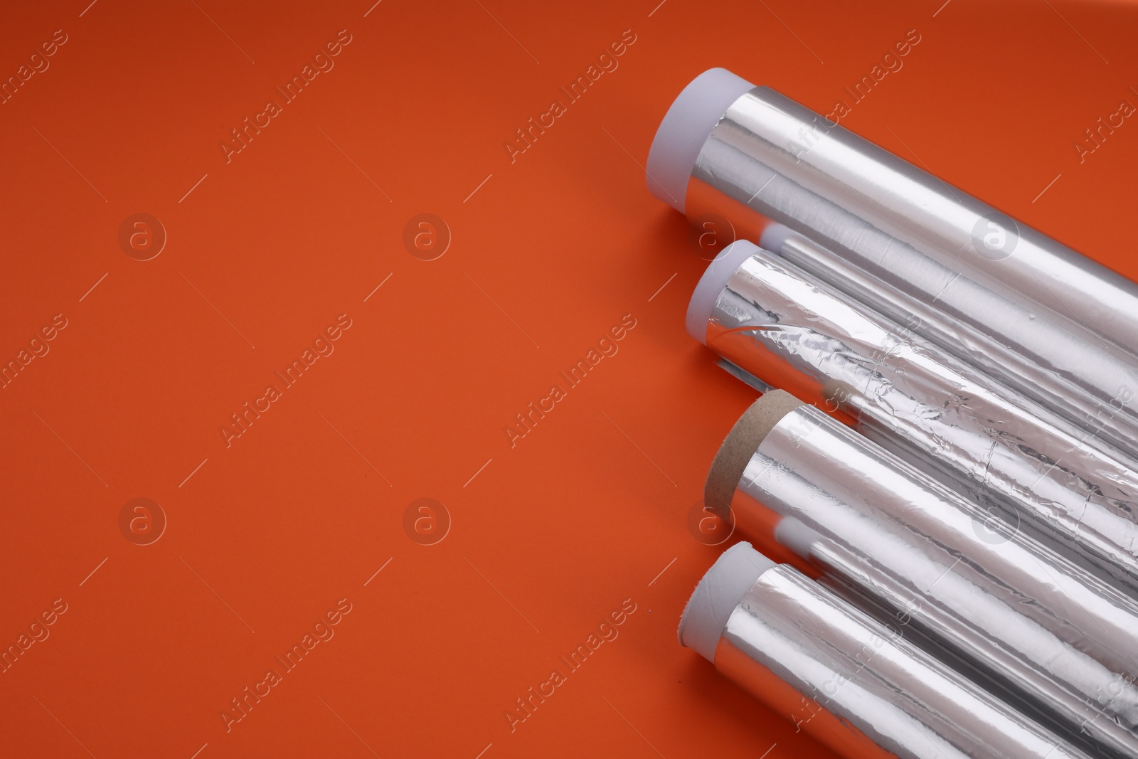 Photo of Rolls of aluminum foil on red background, closeup. Space for text