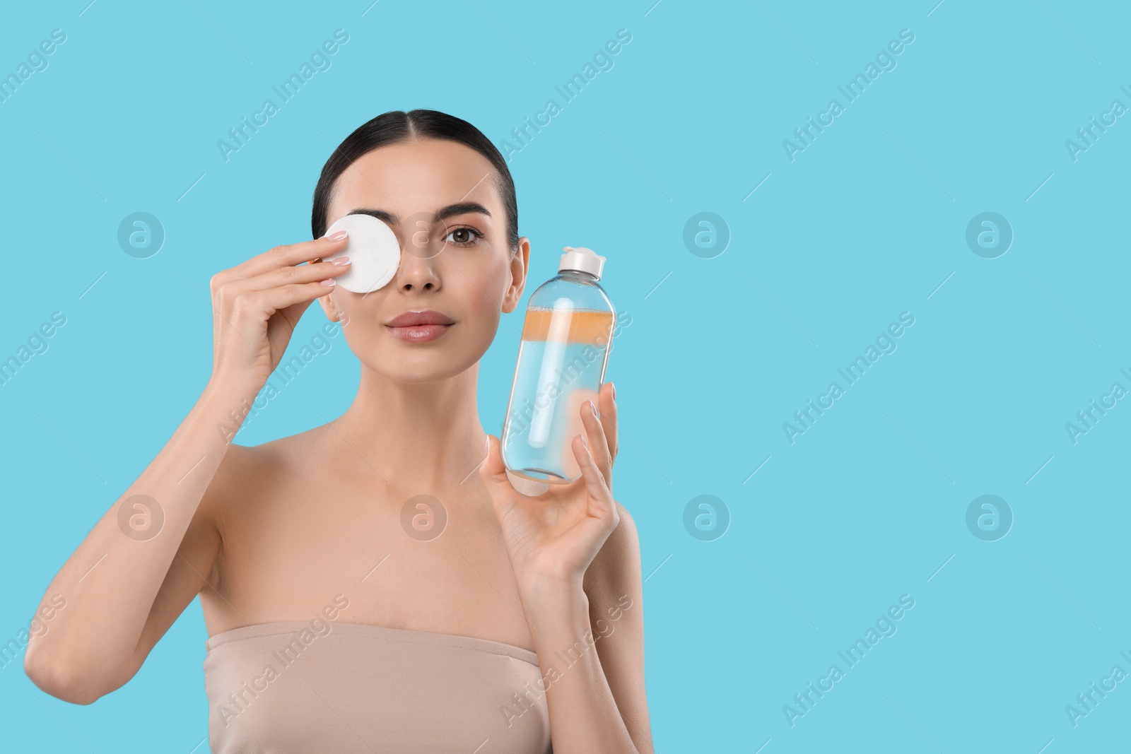 Photo of Beautiful woman removing makeup with cotton pad on light blue background, space for text