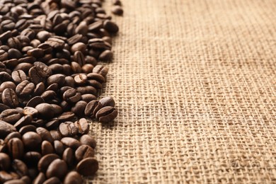 Photo of Many coffee beans on burlap fabric, closeup. Space for text