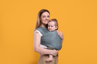 Photo of Mother holding her child in baby wrap on orange background