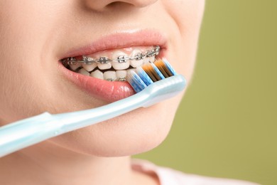 Smiling woman with dental braces cleaning teeth on light green background, closeup