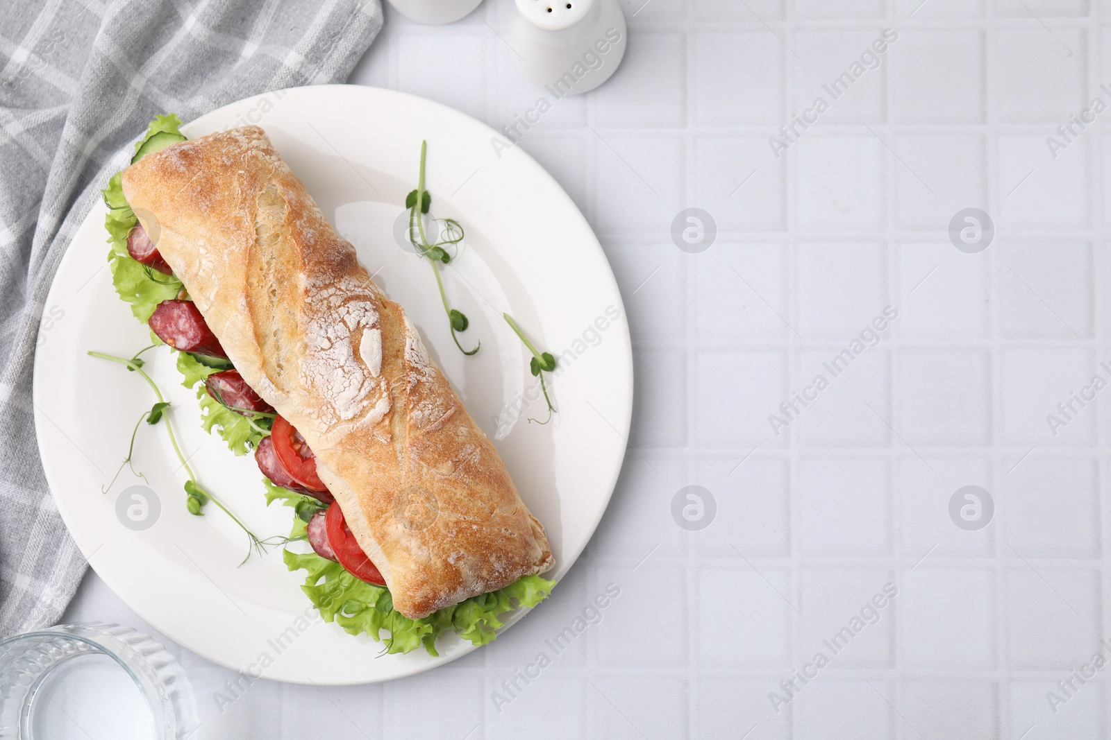 Photo of Delicious sandwich with sausages and vegetables on white tiled table, top view. Space for text