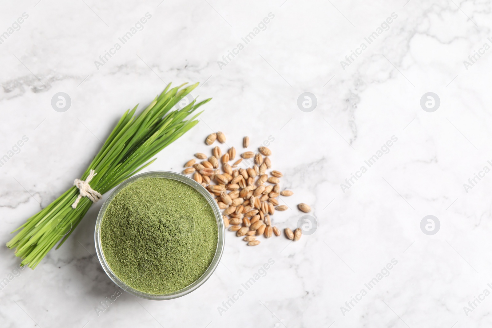 Photo of Wheat grass powder in bowl, seeds and fresh sprouts on white marble table, flat lay. Space for text