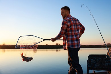 Photo of Fisherman holding fishing net with catch at riverside