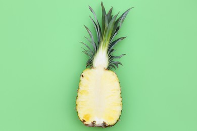 Photo of Half of ripe pineapple on light green background, top view