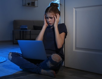 Photo of Terrified teenage girl with laptop on floor in dark room. Danger of internet