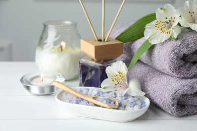 Photo of Spa composition. Towels, burning candles, reed air freshener, sea salt and beautiful flowers on white wooden table, closeup