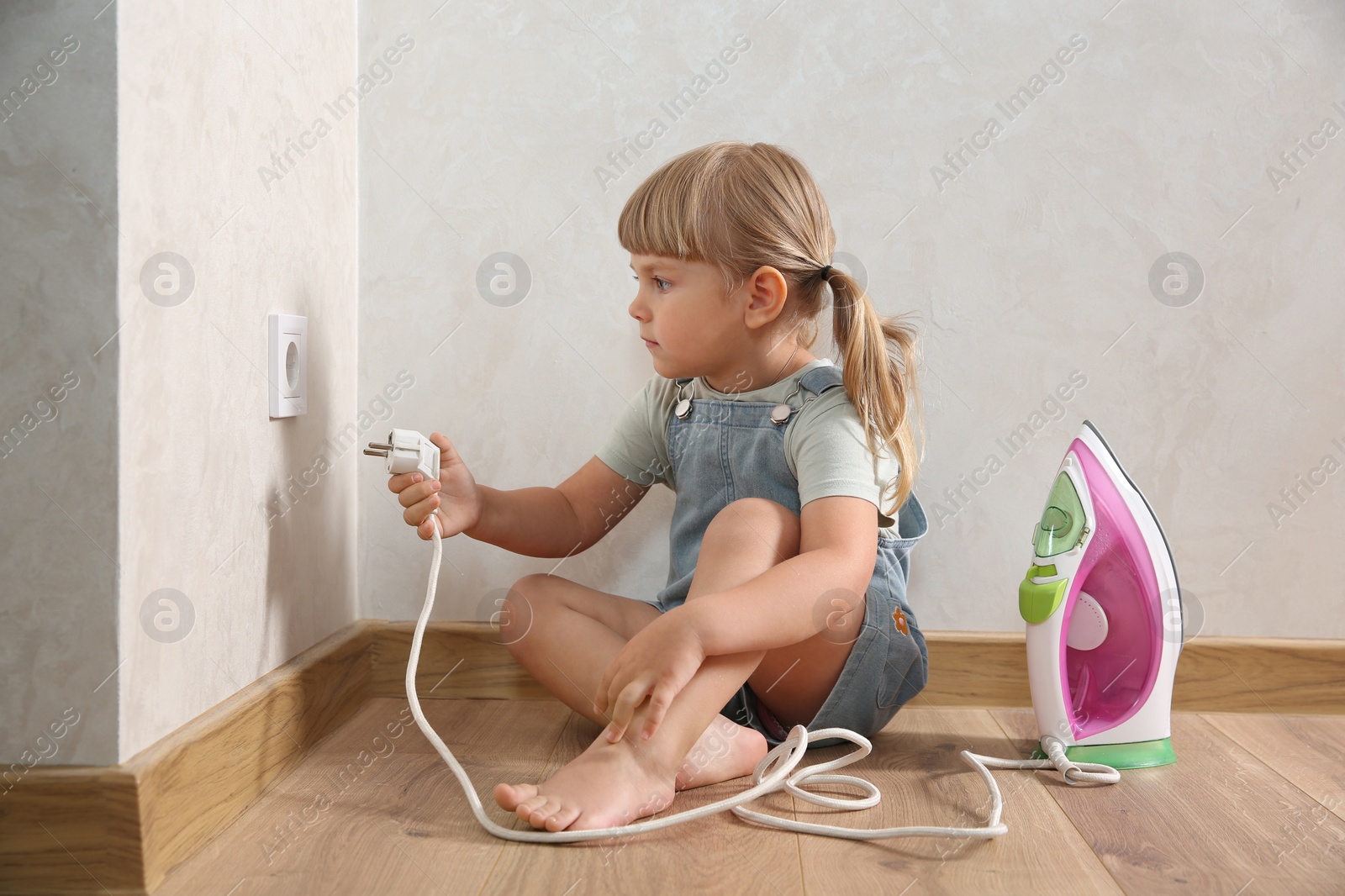 Photo of Little child playing with electrical socket and iron plug at home. Dangerous situation