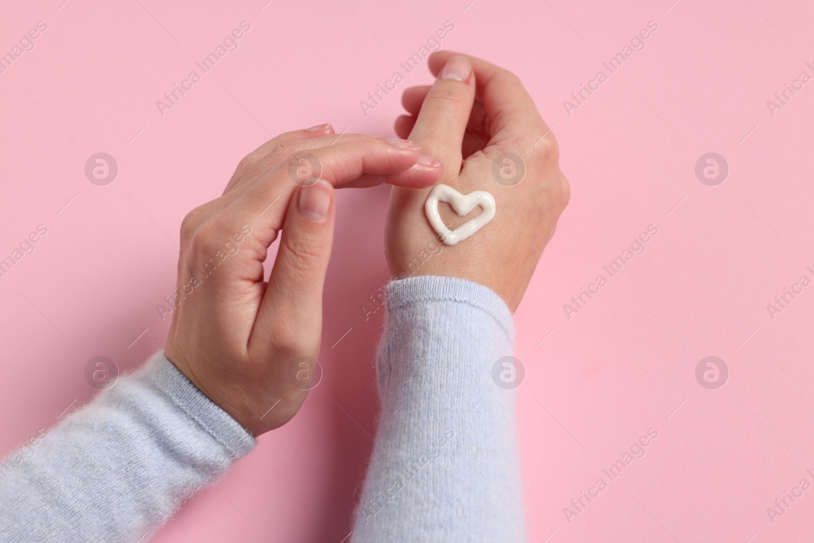 Photo of Woman with heart made of cosmetic cream on hand against pink background, closeup