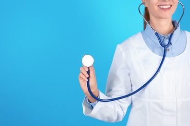 Female doctor holding stethoscope on color background, closeup with space for text