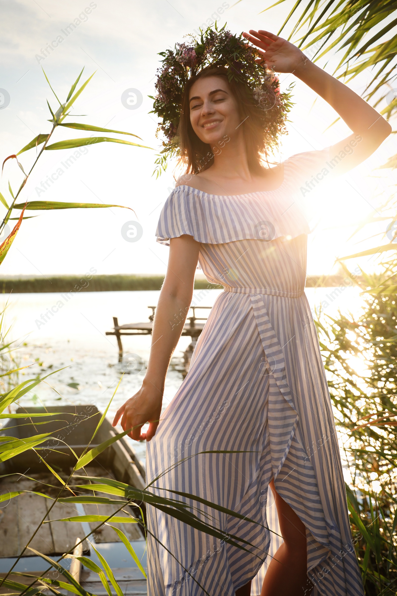 Photo of Young woman wearing wreath made of beautiful flowers near river on sunny day