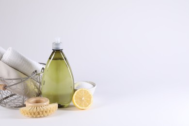 Photo of Bottle of cleaning product, brush, rags and lemon on light background