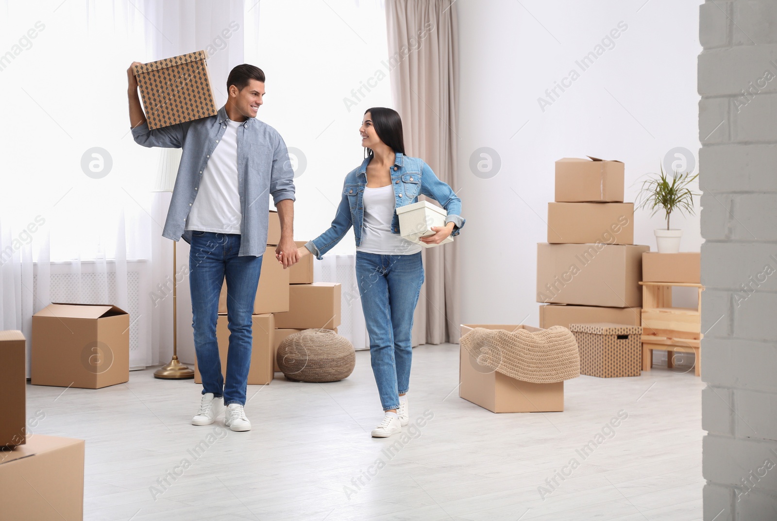 Photo of Happy couple in room with cardboard boxes on moving day