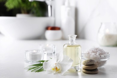 Photo of Essential oils, sea salt, spa stones and orchid flower on white table in bathroom