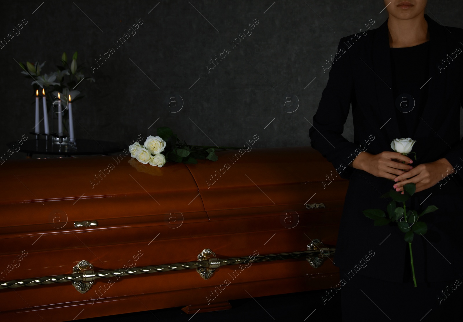 Photo of Young woman with white rose near casket in funeral home, closeup