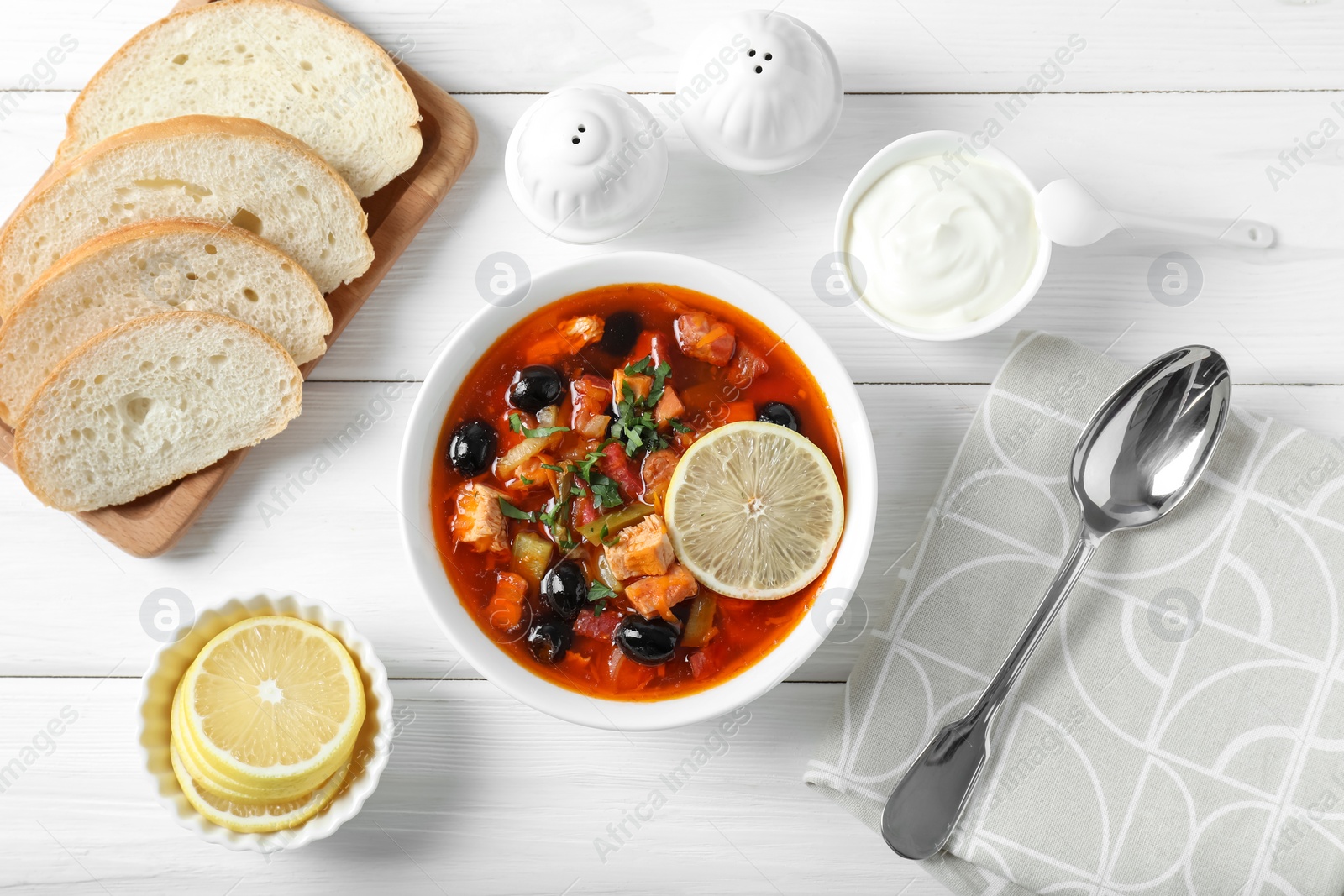 Photo of Meat solyanka soup with sausages, olives and vegetables served on white wooden table, flat lay