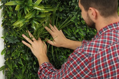 Photo of Man installing green artificial plant wall panel, closeup