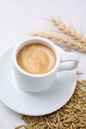 Photo of Cup of barley coffee, grains and spikes on white table, closeup