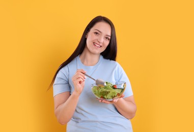 Beautiful overweight woman eating salad on yellow background. Healthy diet