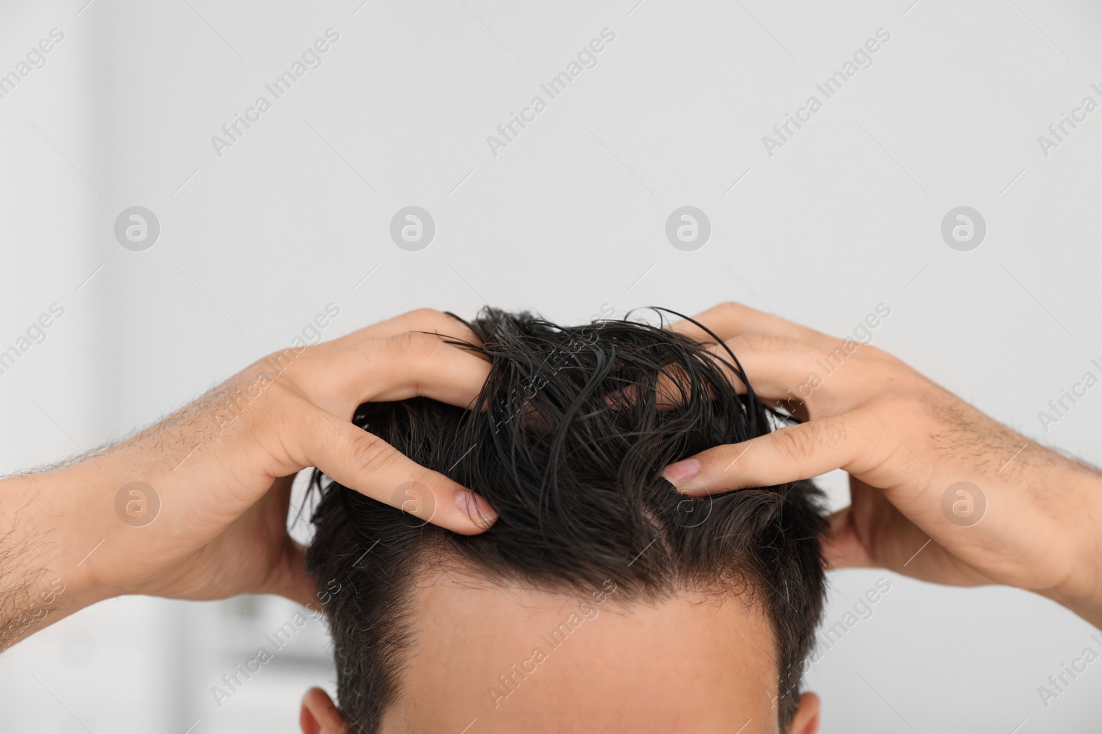 Photo of Man applying hair conditioner against light background, closeup