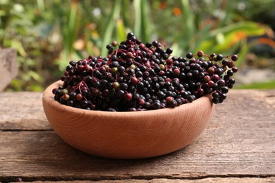 Photo of Bowl with tasty elderberries (Sambucus) on wooden table outdoors, closeup