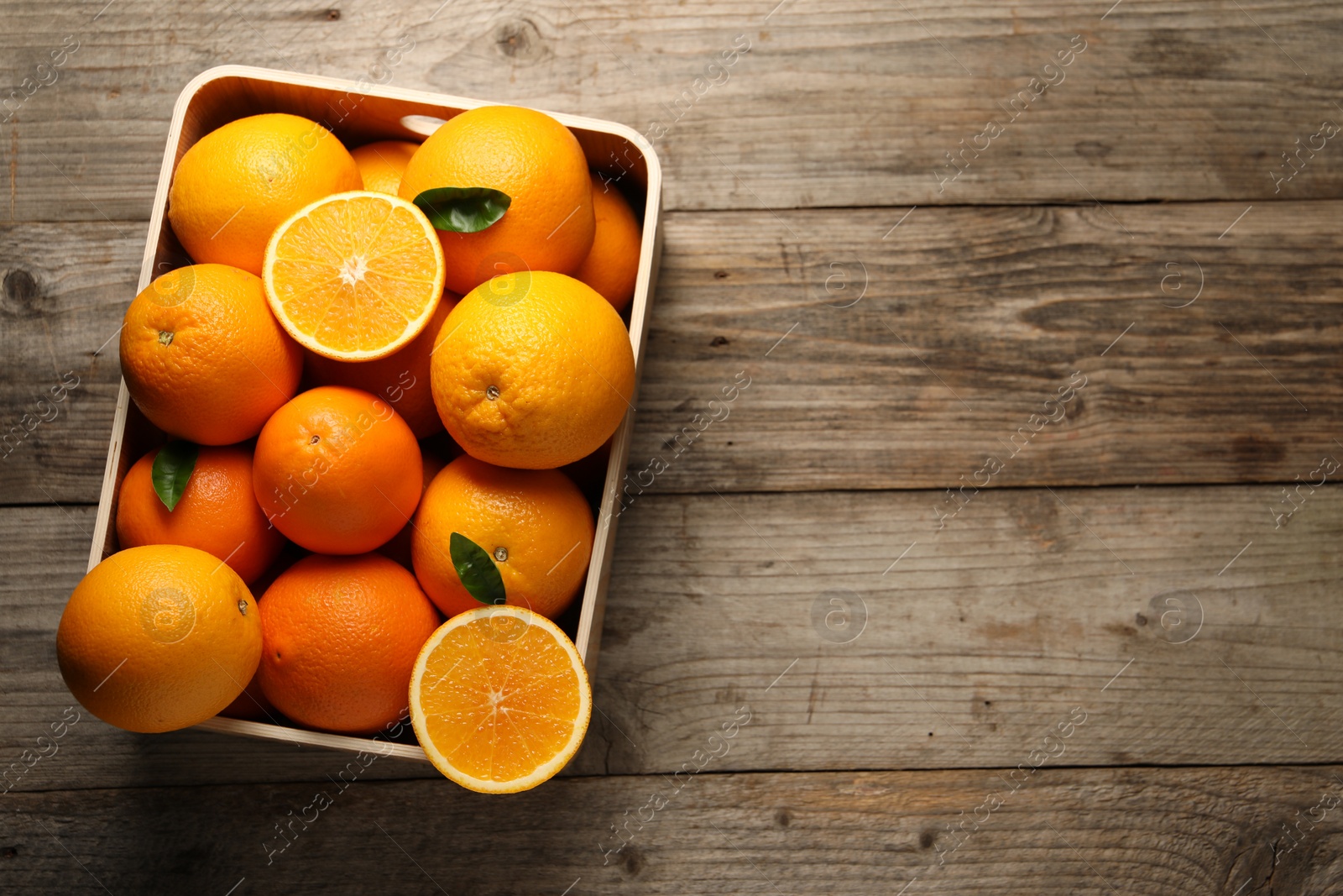 Photo of Many whole and cut ripe oranges on wooden table, top view. Space for text