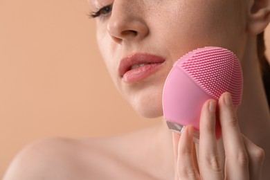 Washing face. Young woman with cleansing brush on beige background, closeup