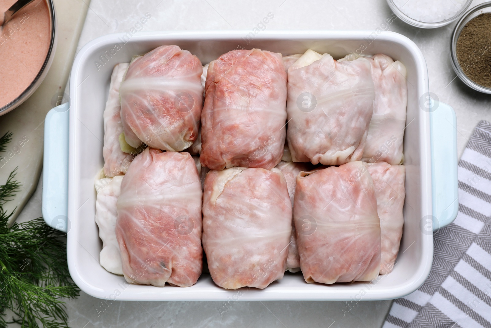 Photo of Uncooked stuffed cabbage rolls in baking dish on light grey table, flat lay