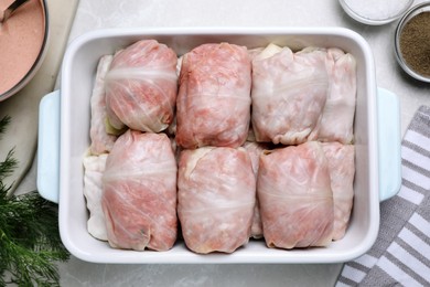 Photo of Uncooked stuffed cabbage rolls in baking dish on light grey table, flat lay