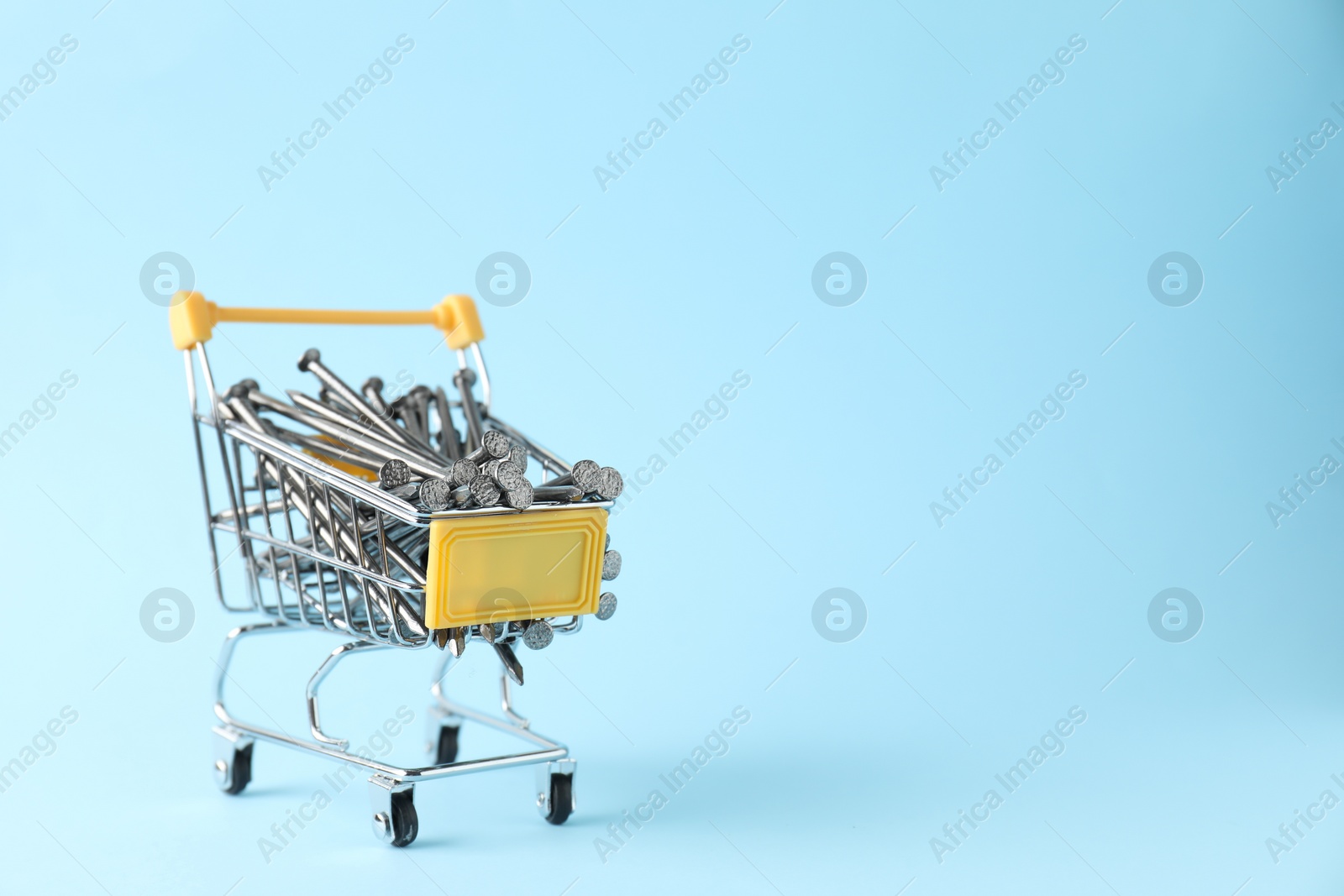 Photo of Metal nails in shopping cart on light blue background, space for text